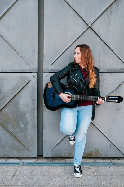 Músico callejero tocando guitarra acústica. Mujer joven con chaqueta al aire libre —  Fotos de Stock