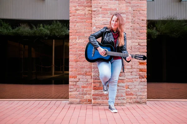 Gatumusiker som spelar akustisk gitarr. ung kvinna bär jacka utomhus — Stockfoto