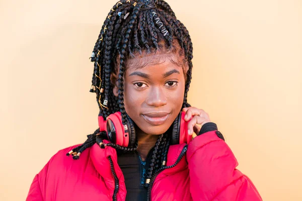 Mooie Afrikaanse vrouw die buiten naar de camera kijkt. Zwarte vrouw luisteren naar muziek met hoofdtelefoon Stockfoto