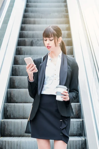 Портрет красивой деловой женщины, использующей смартфон в эскалаторе по дороге на работу — стоковое фото