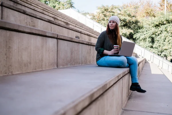 Портрет женщины-фрилансера, использующей ноутбук и пьющей кофе, сидящей на лестнице на городской улице. Концепция блогеров. — стоковое фото