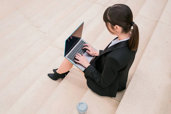 Portrait of beautiful businesswoman using laptop sitting on stairs in city street. — Stock Photo, Image