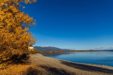Güneşli bir sonbahar gününde Liptovska Mara su deposunun kıyısında tarihi bir beyaz kilise kulesi. Arka planda, Batı ve Yüksek Tatra 'nın karlı zirveleri açık mavi bir gökyüzünün altında görülebilir. Slovakya, Liptov bölgesi.
