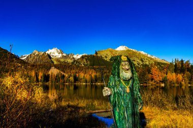 Slovakya 'daki yüksek Tatra dağlarının geniş manzara manzarası. Zirveler, berrak bir gökyüzünün altındaki canlı sonbahar ağaçlarıyla çevrili bir gölün sakin mavi suyuna mükemmel bir şekilde yansıyor..