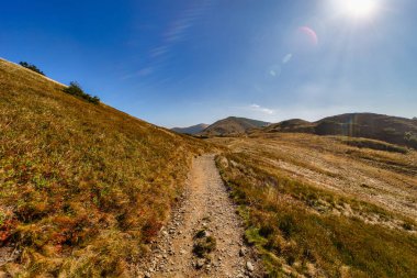 Güneşli bir sonbahar gününde Alçak Tatras Ulusal Parkı 'nın yamaçlarında kıvrılan kayalık bir yürüyüş yolunun geniş panoramik manzarası. Güzel sarı çimenler ve mavi gökyüzü