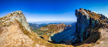 Güneşli bir sonbahar gününde Alçak Tatras Ulusal Parkı 'nın yamaçlarında kıvrılan kayalık bir yürüyüş yolunun geniş panoramik manzarası. Güzel sarı çimenler ve mavi gökyüzü