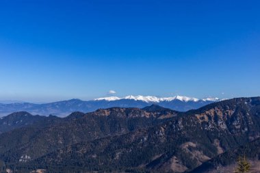 Açık mavi gökyüzünün altındaki karla kaplı dağ sırtlarının nefes kesici panoramik manzarası, ormanlık tepelerden Slovakya 'daki dağlık tepelere geçişi gösteriyor..