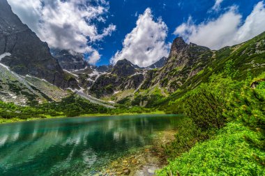 Tarihi dağ kulübesi ve kristal berrak turkuaz suya yansıyan pürüzsüz granit tepeleriyle Zelene pleso 'nun (Yeşil Göl) göz kamaştırıcı geniş manzarası. Yüksek Tatras Ulusal Parkı, Slovakya.