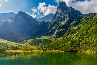 Zelene Pleso 'nun zümrüt sularına yansıyan Jastrabia veza dağ zirvesinin güçlü bir görüntüsü. Slovakya 'da parlak bir yaz gökyüzünün altında yemyeşil çam çalıları ve dik granit duvarlar.
