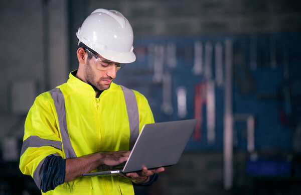 Chief Engineer in the Hard Hat Walks Through Light Modern Factory While Holding Laptop. Successful, Handsome Man in Modern Industrial Environment.