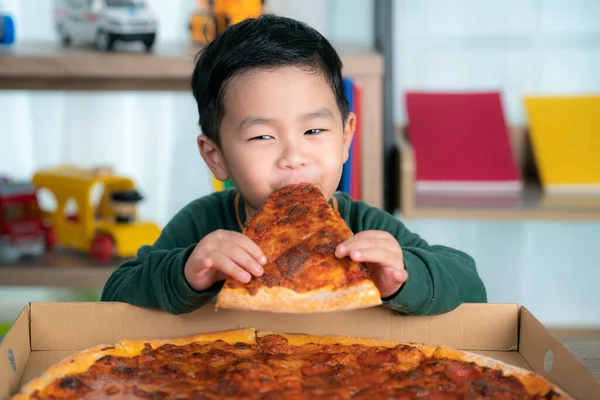 Asian boy eating pizza and pizza box put on the table.