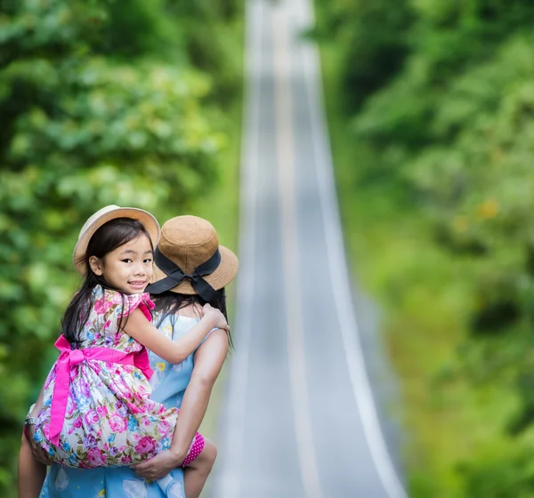 Liten glad tjej som njuter av en piggyback rida på ryggen mödrar — Stockfoto