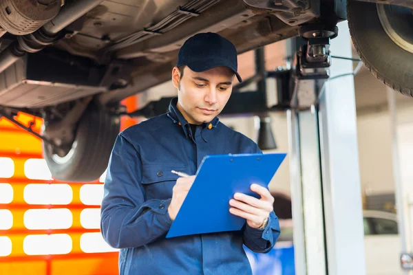 Mechanic taking notes under car — Stock Photo, Image