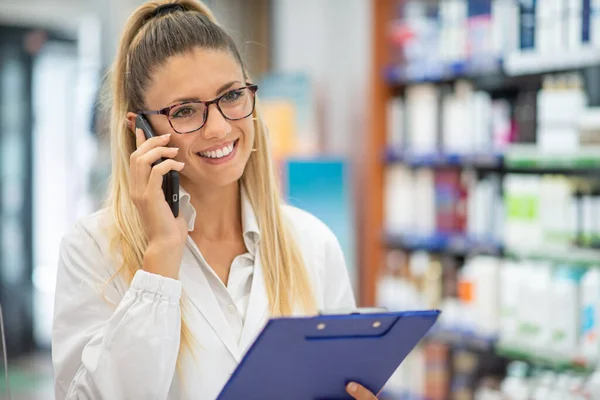 Smiling Female Pharmacist Talking Phone While Reading Prescription Her Pharmacy — kuvapankkivalokuva