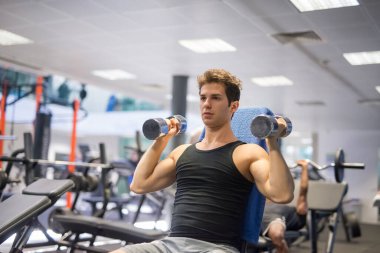 Vücut geliştirici, spor salonunda kollarını çalıştırmak için dambıl kullanıyor.