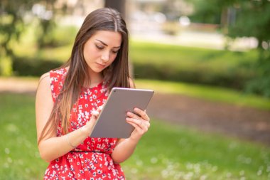 Parkta dijital tablet kullanan genç bir kadın.
