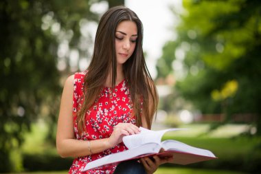 Parkta kitap okuyan kız öğrenci.