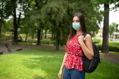 Parkta yürüyen maskeli kadın öğrenci, Coronavirus covid-19 eğitim konsepti