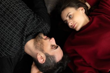 Mutlu, rahat, çekici bir adam ve kadın siyah bir halıya sırtüstü uzanmış gülümsüyor.