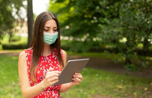 公園でタブレットを使用してマスクの若い女性 — ストック写真