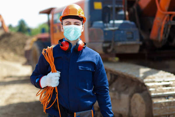 Portrait of masked worker in a construction site, covid coronavirus construction concept
