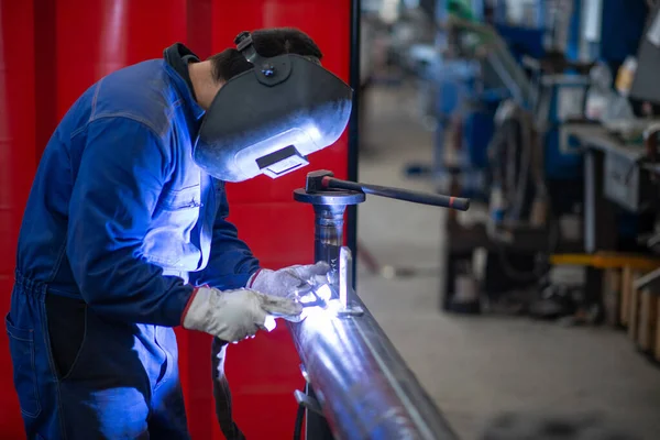 Welder at work in a production facility, man welding an iron or steel pipe