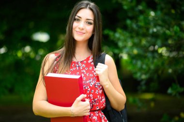 Güzel bir kız öğrenci açık havada kitap tutuyor.