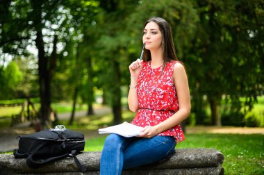 Güzel bir üniversite öğrencisi parkta bir bankta kitap okuyor.