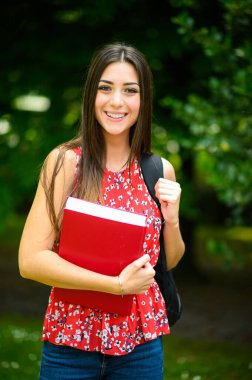 Güzel bir kız öğrenci açık havada kitap tutuyor.