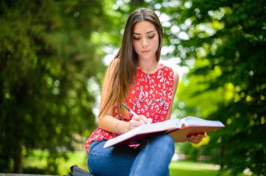 Güzel bir üniversite öğrencisi parkta bir bankta kitap okuyor.