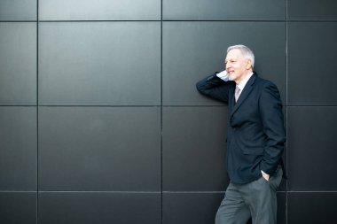 Kıdemli yakışıklı işadamı siyah bir duvarın yanında dikiliyor.