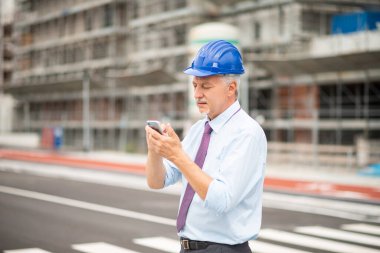 İnşaat alanının önünde cep telefonunu kullanan mimar.