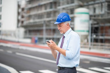 İnşaat alanının önünde cep telefonunu kullanan mimar.