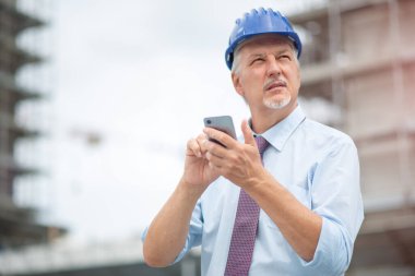 İnşaat alanının önünde cep telefonunu kullanan mimar.