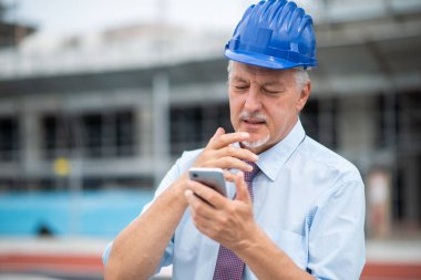 İnşaat alanının önünde akıllı telefonunu kullanan bir mimar.