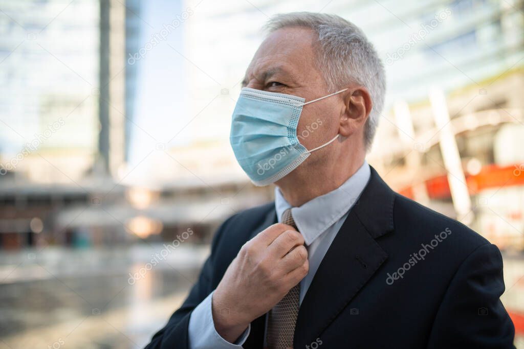 Senior manager adjusting his necktie while walking outdoor wearing a mask during coronavirus and covid pandemic