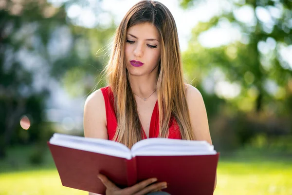 公園に座って本を読んでいる若い女性 — ストック写真