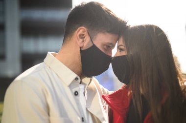 Romantik mutlu genç çift, yakın bir kucaklaşmada birbirlerinin gözlerinin içine bakıyorlar. Alınları, Coronavirus Covid 19 salgınına karşı maske takıyor ve birbirlerine dokunuyorlar.