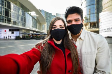 Koronavirüs salgınını önlemek için dışarıda birlikte resim çektiren ve maske takan genç bir çift.