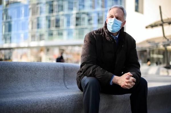 老人は屋外に座っているコロナウイルスのパンデミックに対する保護マスクを着て — ストック写真