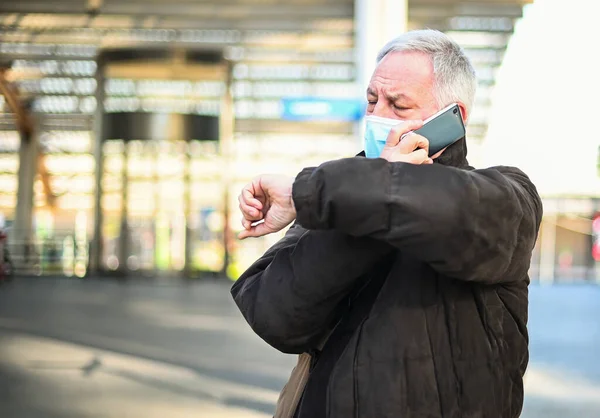 携帯電話の屋外のシニア男とマスクを身に着けている間の時間をチェック コロナウイルスの概念 — ストック写真