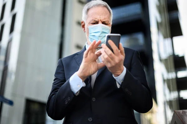 コロナウイルスのパンデミックから保護するためにマスクを身に着けている間 彼のスマートフォンの屋外を使用してシニアマネージャー — ストック写真