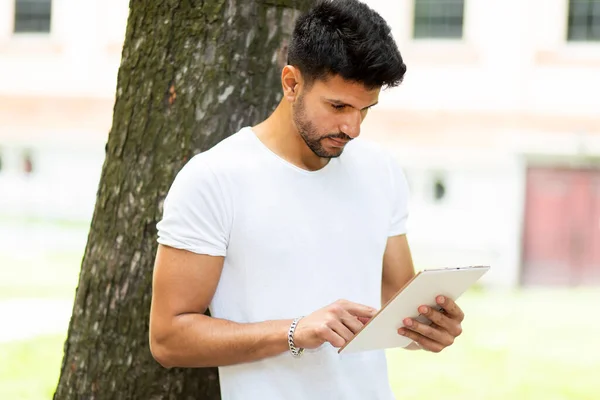 Joven Usando Una Tableta Digital Tumbado Contra Árbol Parque Disfrutando — Foto de Stock