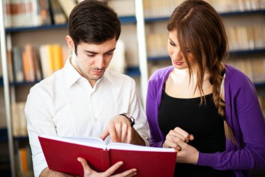 Birkaç öğrenci kütüphanede kitap okuyor.