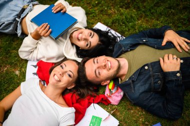 Üç öğrenci çimenlerde yatıp gülümsüyor.