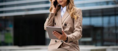 Genç iş kadını elinde tablet tutarken cep telefonunu kullanıyor.