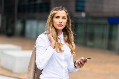 İş kadını cep telefonunu açık havada kullanıyor.