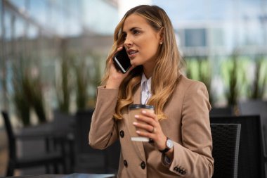 Genç sarışın iş kadını bir kafede telefonla konuşuyor.
