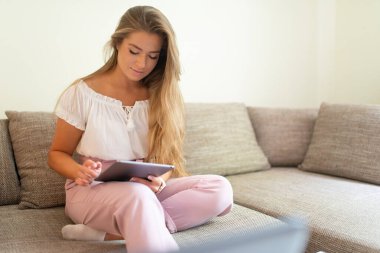 Evindeki kanepede dinlenirken tablet kullanan bir kadın.