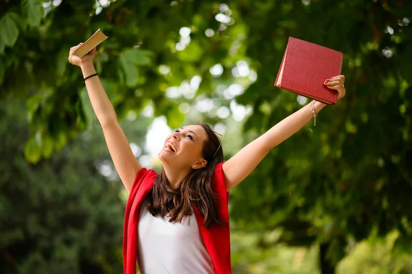 Excited student girl raising books up celebrating outdoors
